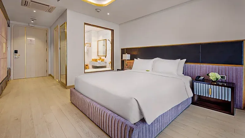 Phòng ngủ Corner Suite tại Danang Golden Bay với giường lớn, đầu giường bọc nhung và chi tiết viền vàng