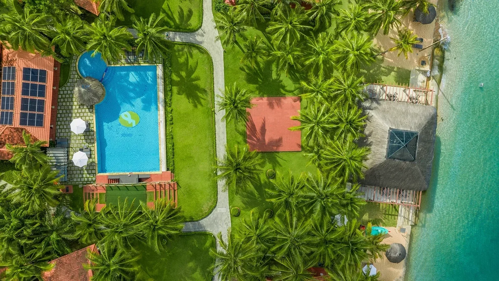 Famiana Resort & Spa nhìn từ trên cao: hồ bơi giữa bãi cỏ, lối đi lát đá, rặng dừa và nhà hàng mái lá sát nước biển xanh