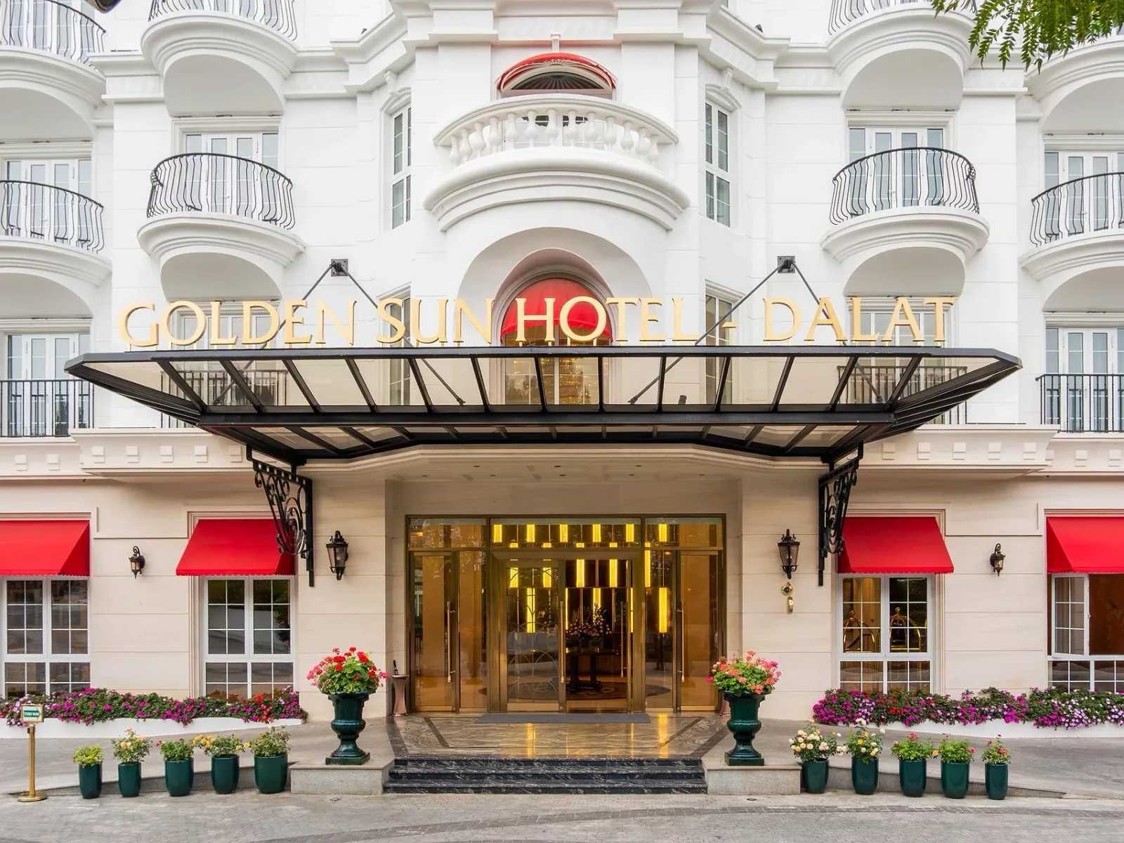 Mặt tiền Golden Sun Hotel Dalat màu trắng với ban công sắt, mái kính sảnh và bảng tên vàng