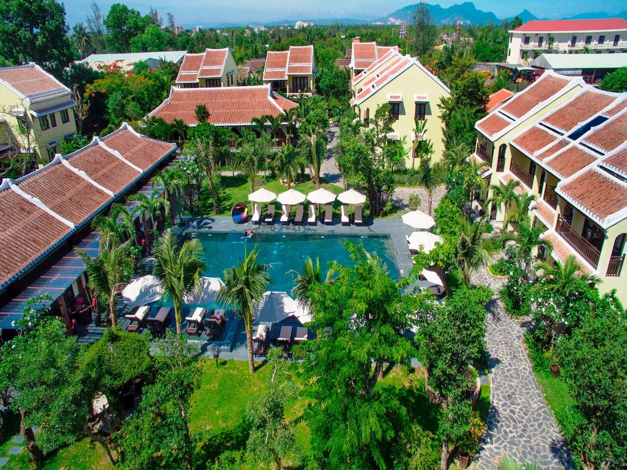 Toàn cảnh Hoi An Silk Village Resort & Spa từ trên cao: các dãy nhà vàng mái ngói đỏ quây quanh hồ bơi và vườn dừa