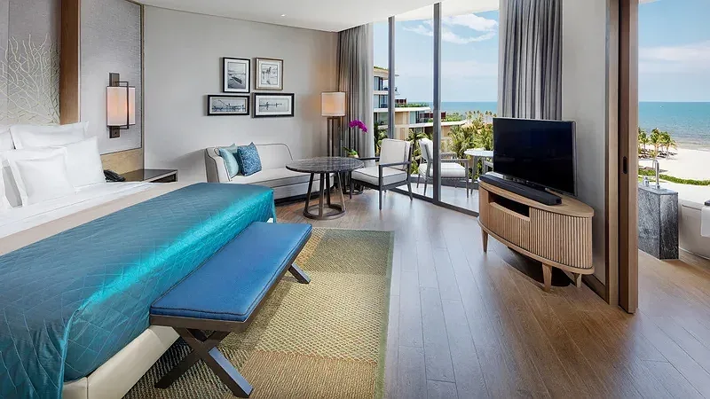Phòng Resort Classic Ocean View tại InterContinental Phu Quoc Long Beach Resort với giường phủ xanh ngọc và cửa kính nhìn ra biển