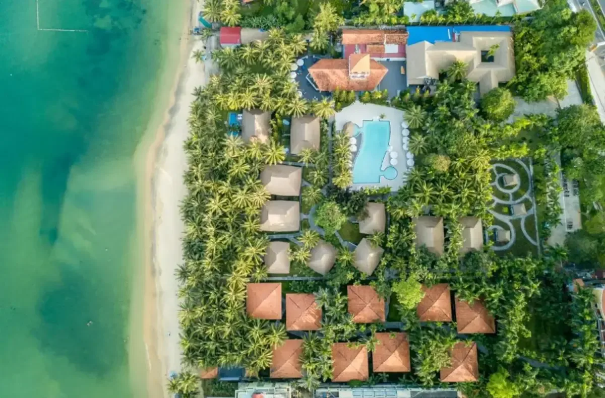 L'Azure Resort & Spa nhìn thẳng từ trên cao: các bungalow mái nâu giữa vườn dừa, hồ bơi ở giữa và dải cát chạy sát mép nước