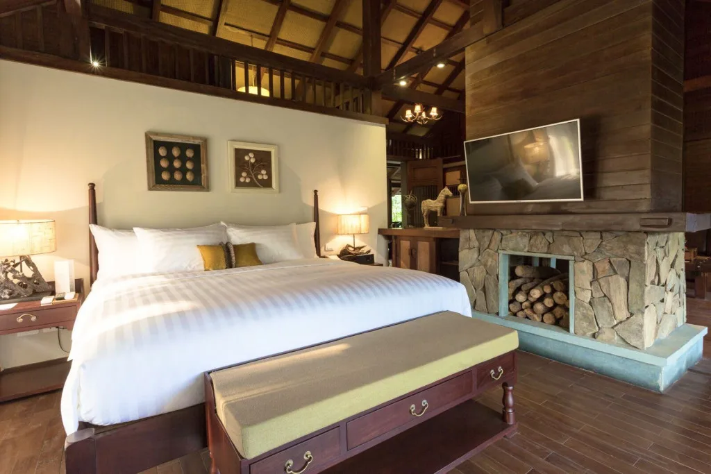 Villa Suite Lò Sưởi tại Le Mont Bavi Resort & Spa với giường lớn, trần gỗ cao và lò sưởi đá xếp củi