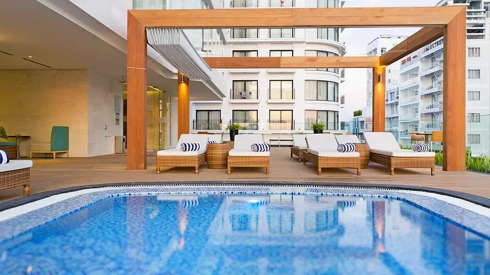 Hồ bơi tầng thượng Liberty Central Nha Trang Hotel với ghế mây nằm dưới giàn gỗ, phía sau là các tòa nhà trong phố