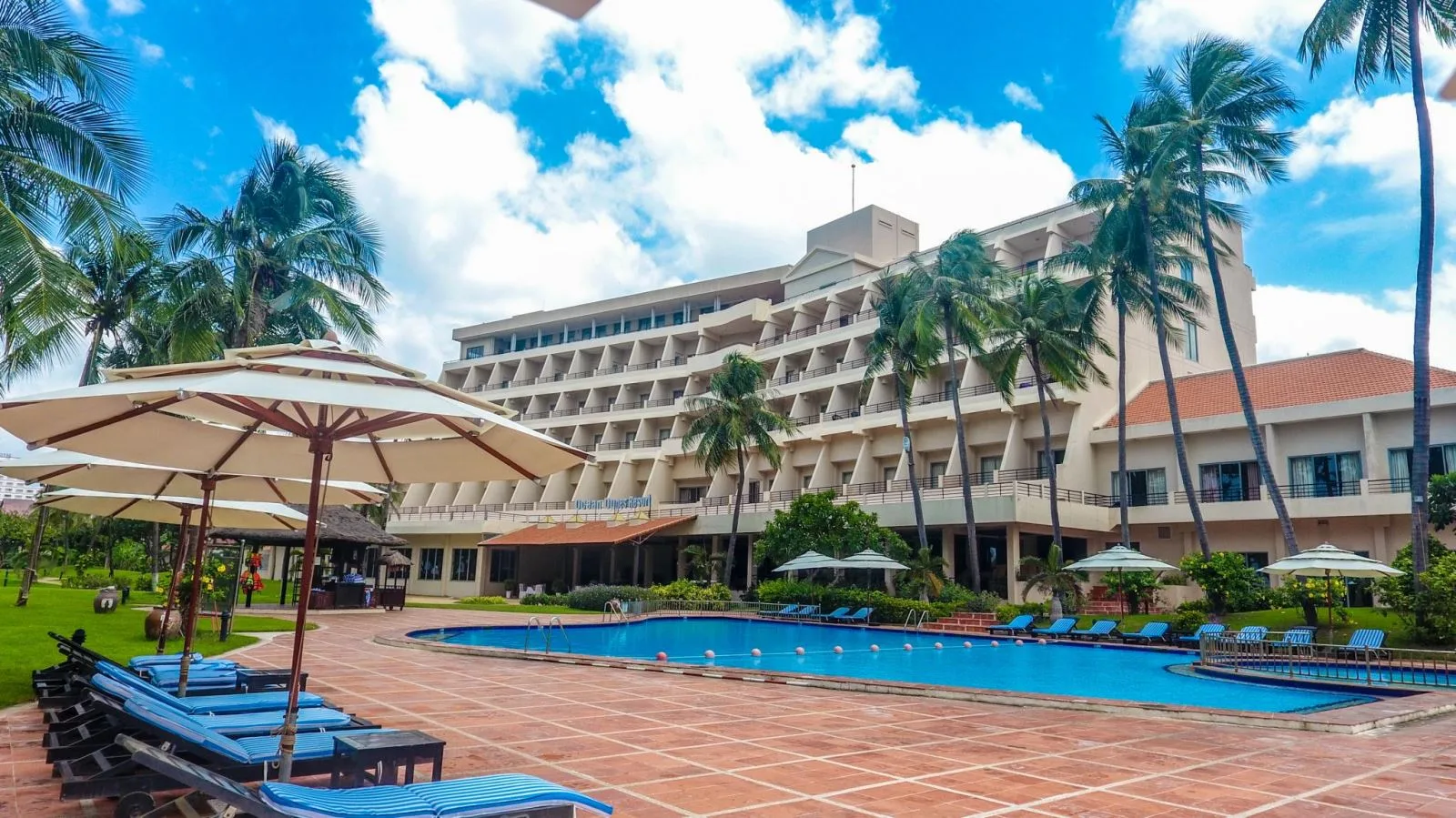 Toà nhà chính Phan Thiet Ocean Dunes Resort nhiều tầng có ban công, hồ bơi và hàng ghế tắm nắng xanh dưới hàng dừa