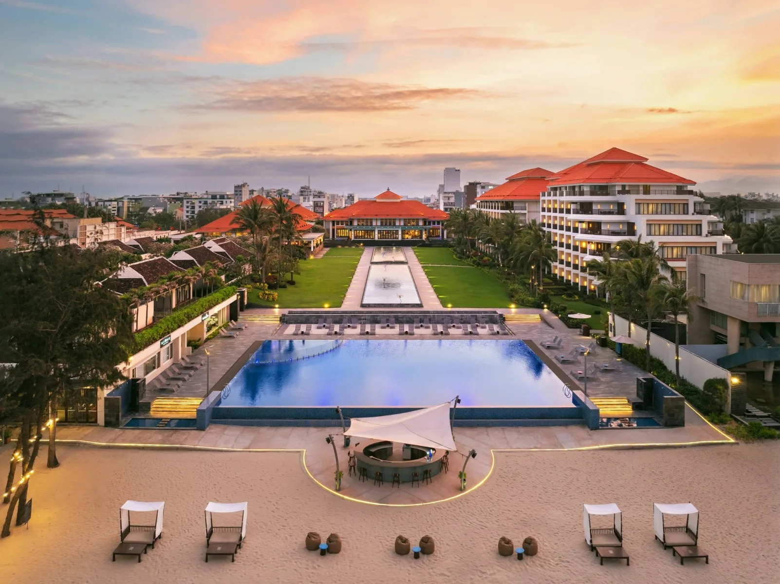 Toàn cảnh Pullman Danang Beach Resort lúc hoàng hôn với mái ngói đỏ, bể bơi lớn và bãi cát ven biển