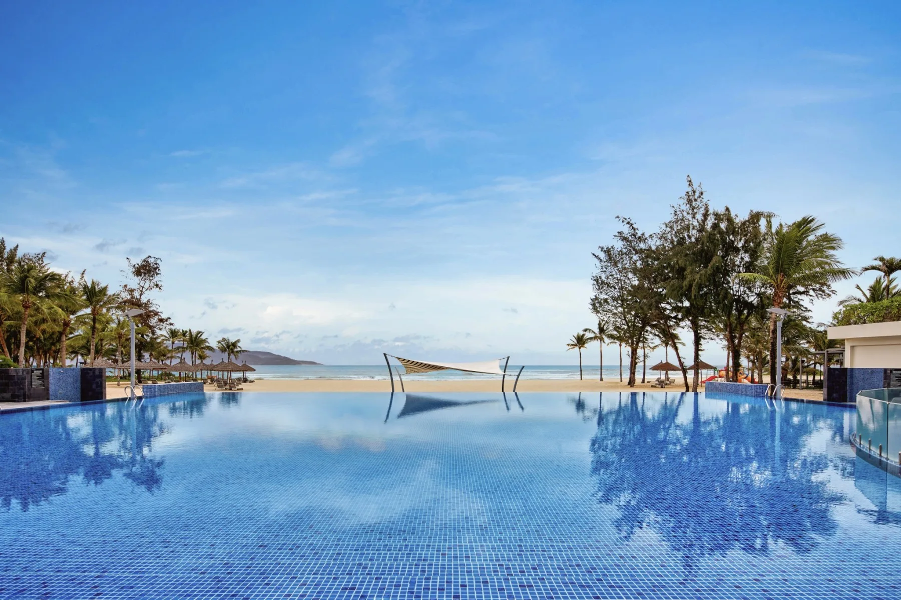 Hồ bơi vô cực của Pullman Danang Beach Resort nhìn thẳng ra bãi cát và biển, hai bên là hàng cây