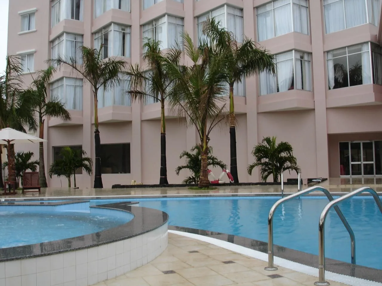 Hồ bơi ngoài trời của Sài Gòn Kim Liên Resort, hàng dừa trước tòa nhà sơn hồng