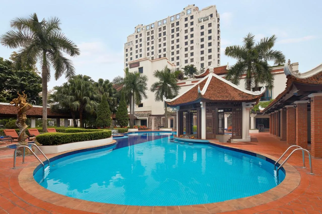 Bể bơi ngoài trời Sheraton Hanoi Hotel giữa hàng cọ, nhà mái đình kiểu Á Đông và toà khách sạn phía sau