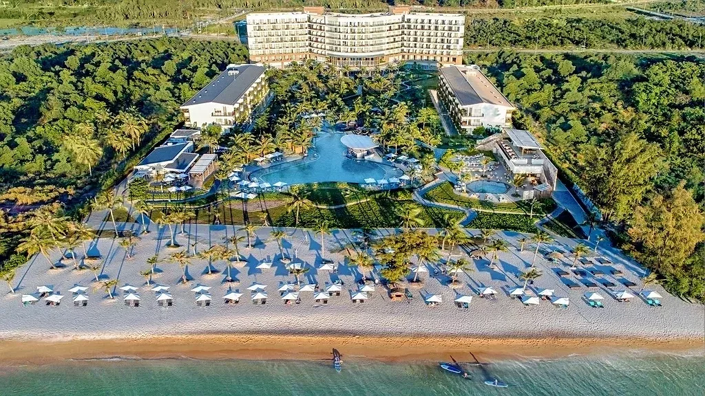 Sol by Meliá Phú Quốc nhìn từ trên cao: dãy ghế và dù trắng trên bãi cát, cụm bể bơi lớn giữa hàng dừa và các khối nhà phía sau