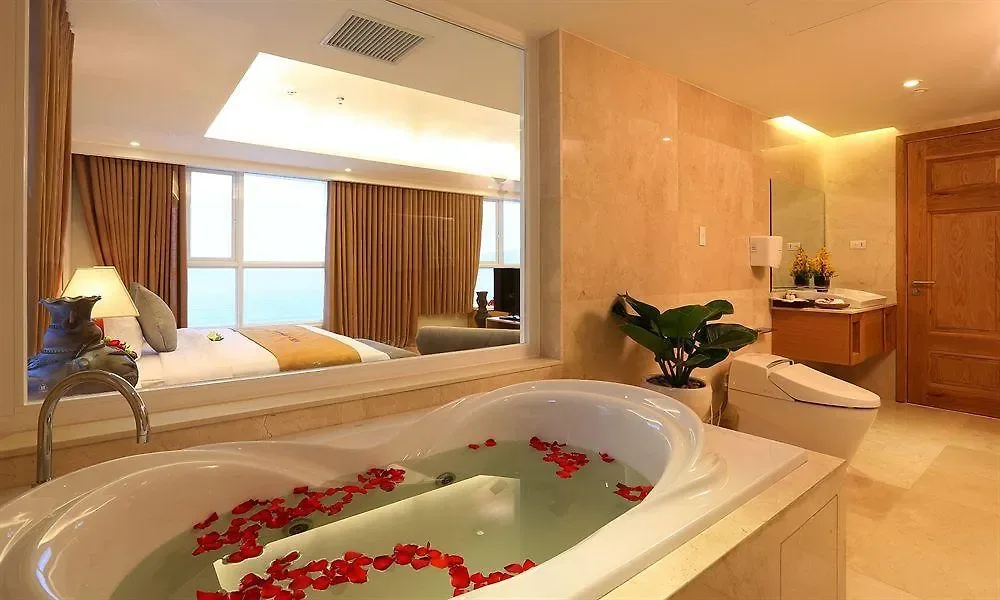Bồn sục hình trái tim rải cánh hoa hồng, vách kính nhìn sang giường và cửa sổ hướng biển trong Honeymoon Suite Bồn Sục tại VDB Nha Trang