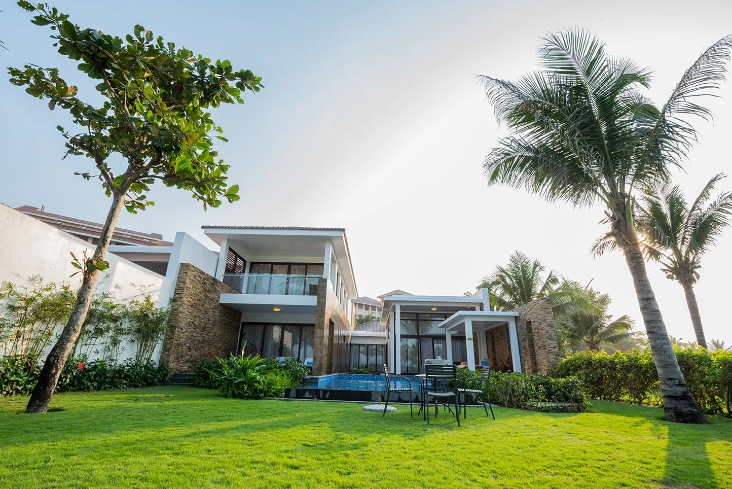 Biệt thự Vinpearl Luxury Da Nang hai tầng với hồ bơi riêng, bàn ghế ngoài trời trên bãi cỏ và hàng dừa